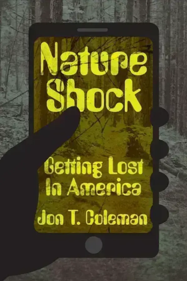 A hand holds a smartphone displaying the book cover "Nature Shock: Getting Lost In America" by Jon T. Coleman, over a forest background.